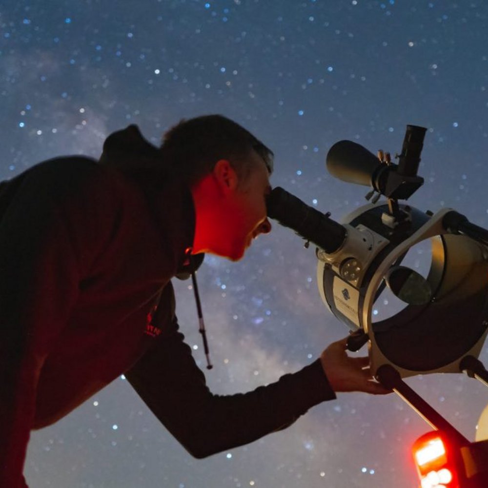 Serata di Astronomia Umbria Assisi con Cena sotto le Stelle Persona che osserva le stelle attraverso un telescopio di notte