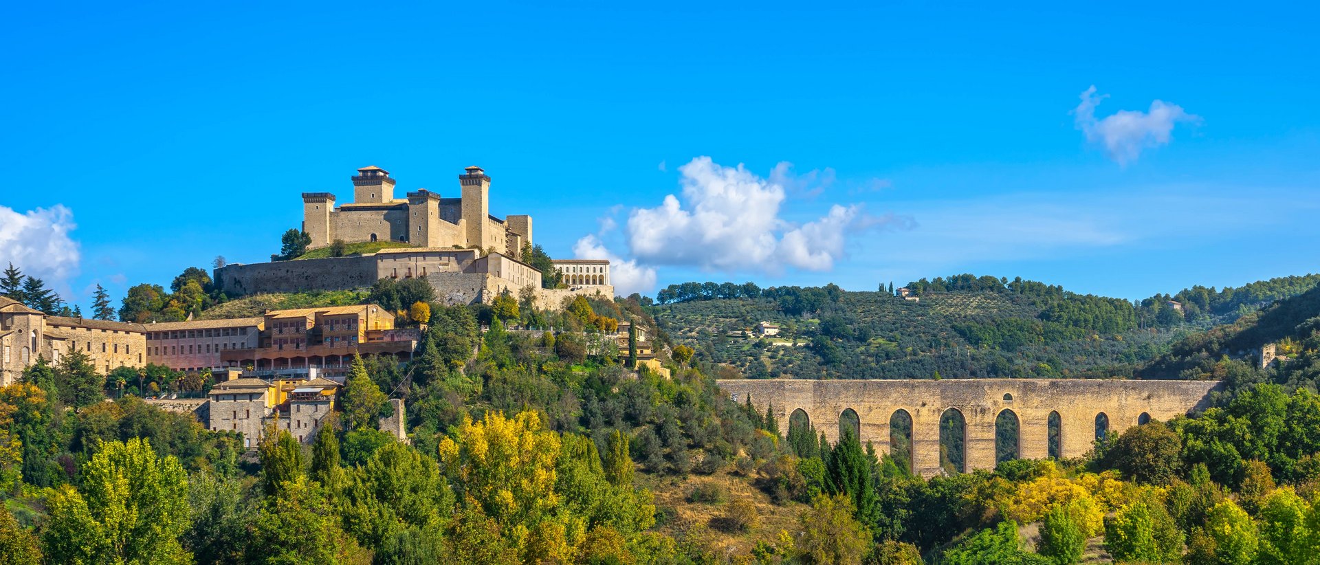 Basilica of Saint Francis of Assisi Medieval castle and aqueduct on green hill under blue sky