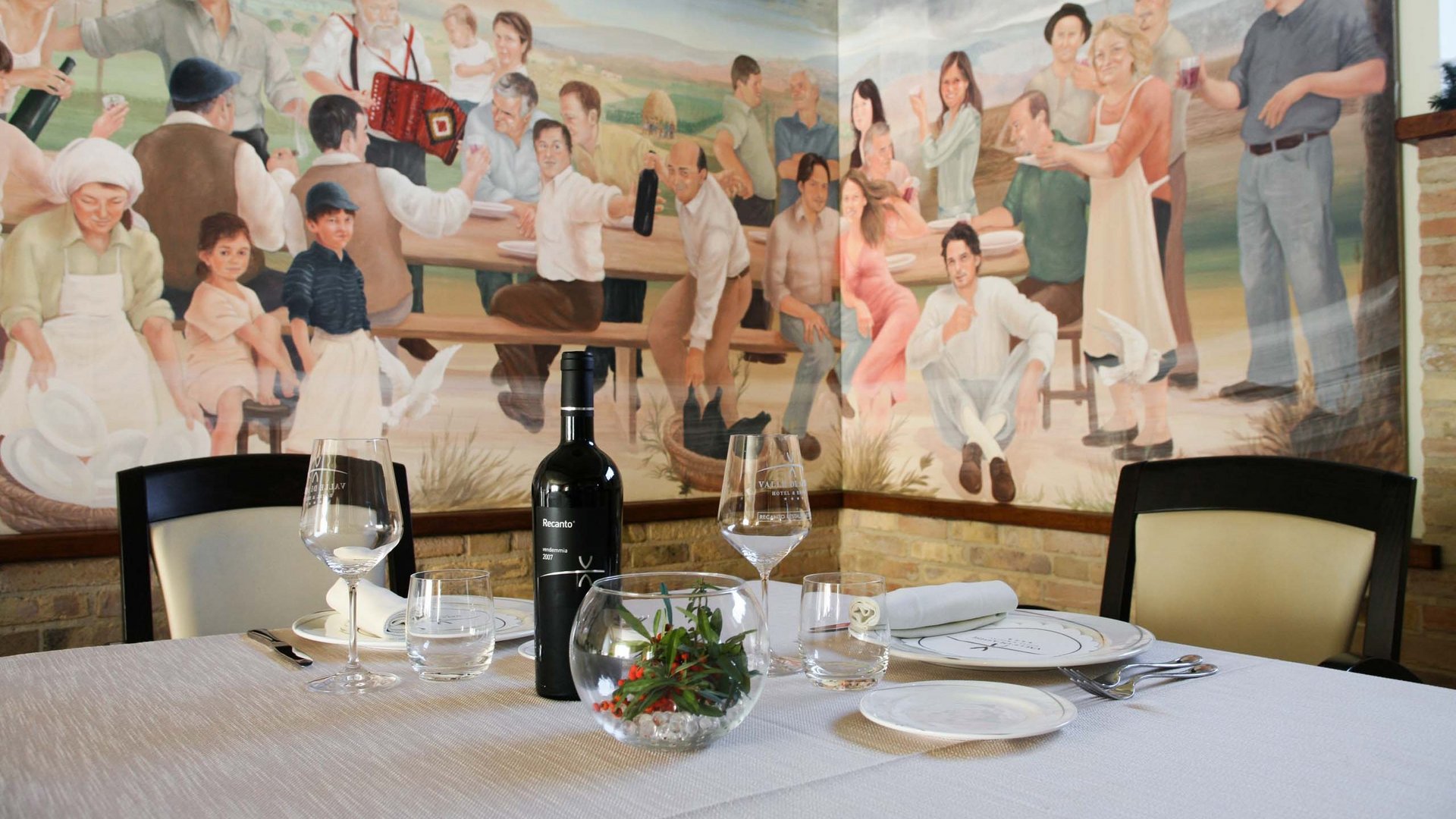 Umbrien: Unterkunft mit Restaurant Eingerichteter Tisch mit Wein vor Wandgemälde von feiernden Menschen