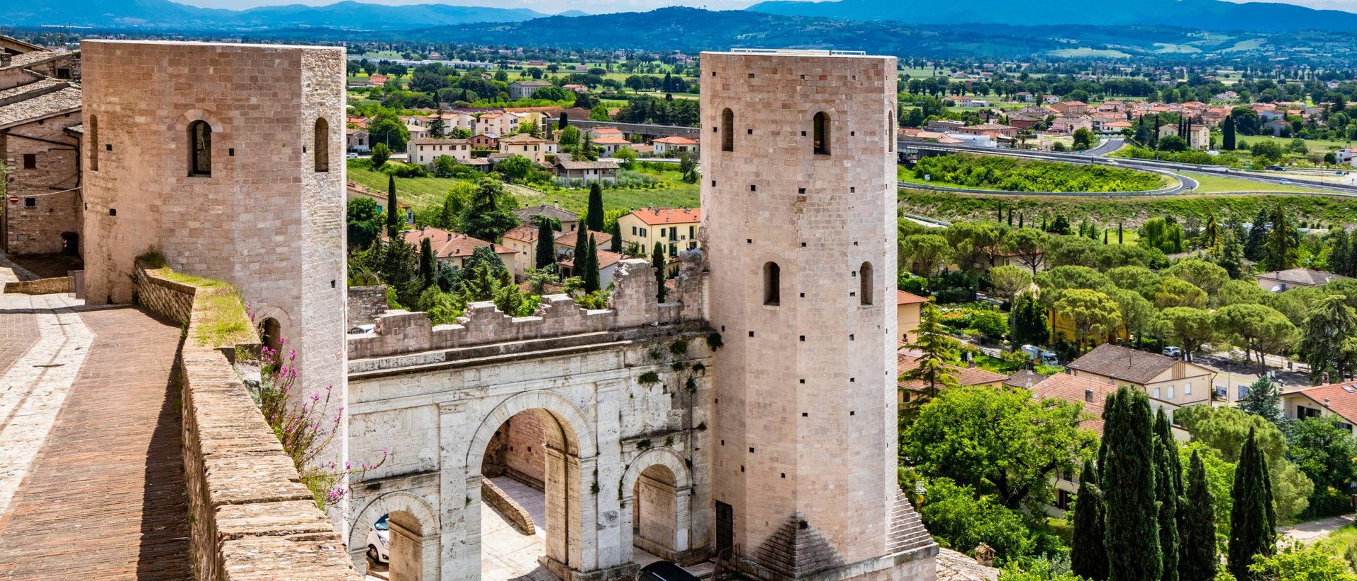 Basilica of Saint Francis of Assisi View of medieval gate with two stone towers and green landscape around