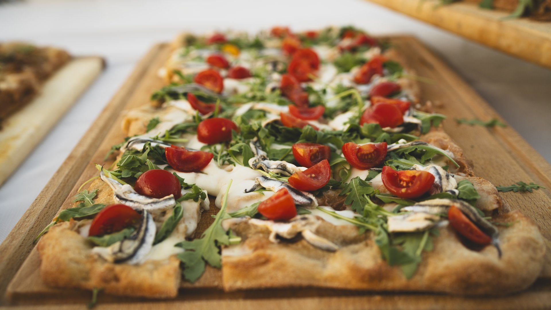 Cena Sotto le Stelle Pizza rettangolare con pomodorini, rucola e mozzarella su tagliere di legno