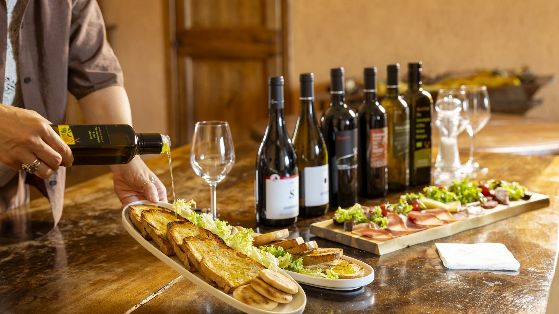 Assisi: Unterkunft mit Restaurant Person gießt Olivenöl auf geröstetes Brot mit Weinflaschen und Vorspeisen auf dem Tisch