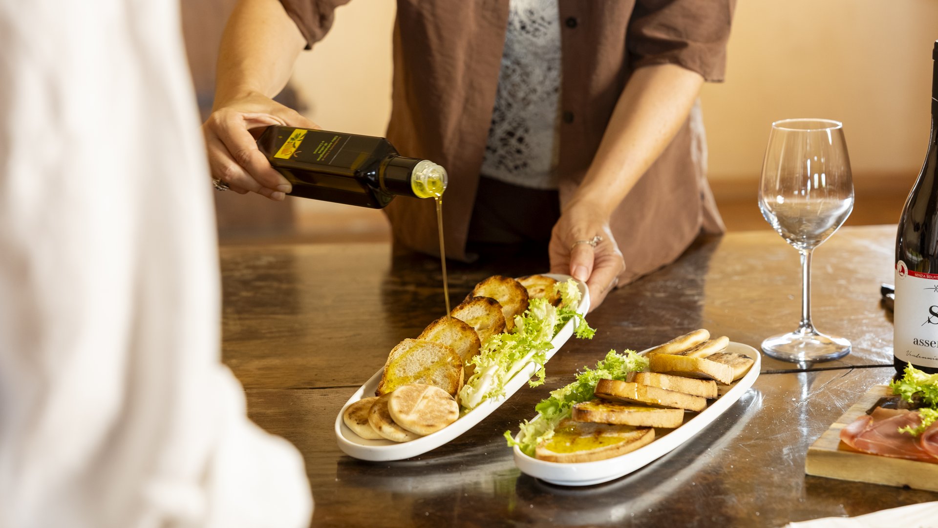 Ferienhäuser in Umbrien und Bio-Bauernhof Person gießt Olivenöl auf geröstete Brotscheiben mit Salat auf weißen Tellern