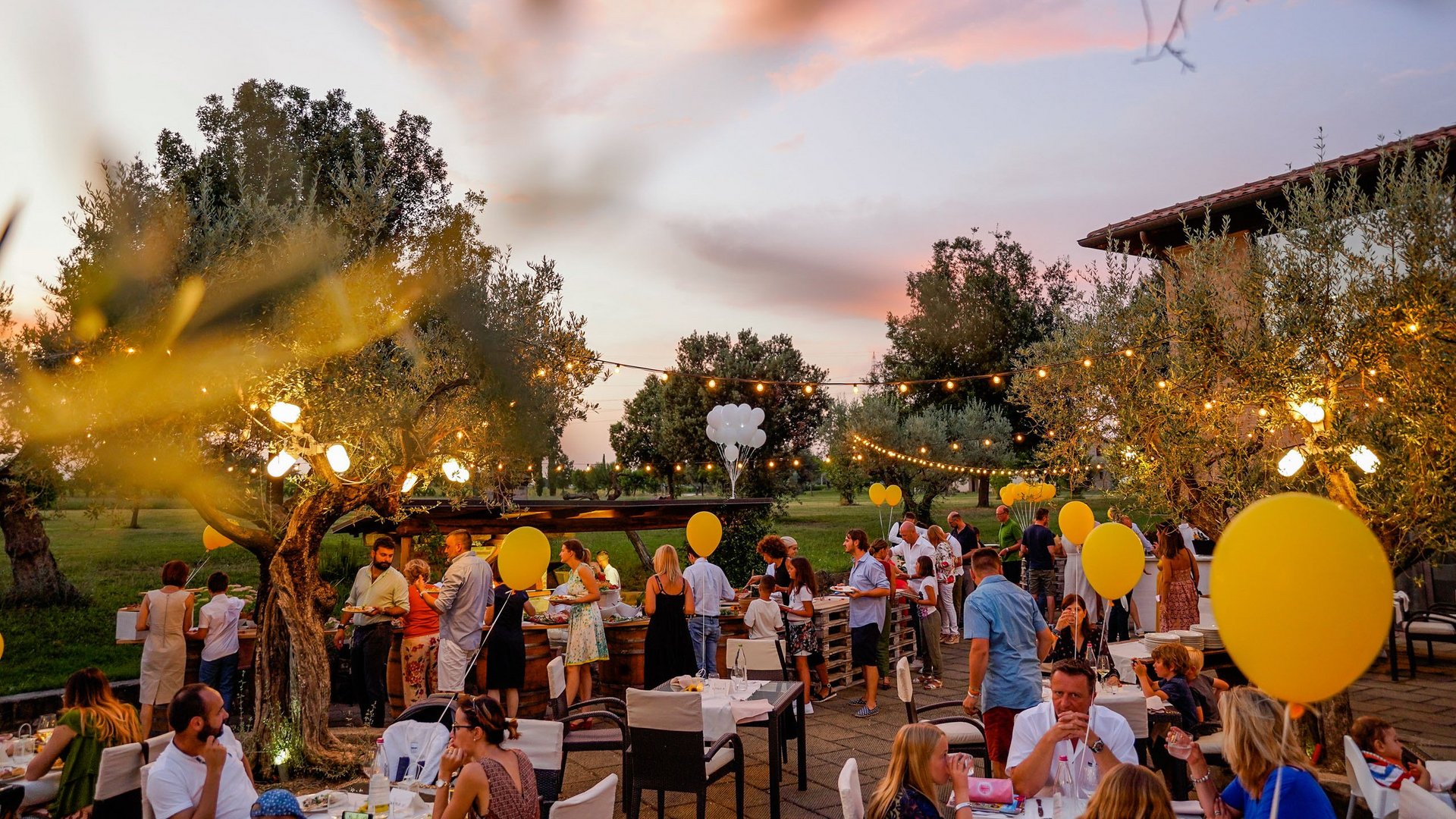Sala Eventi all'aperto vista Assisi Festa all'aperto di sera con palloncini gialli e persone che socializzano